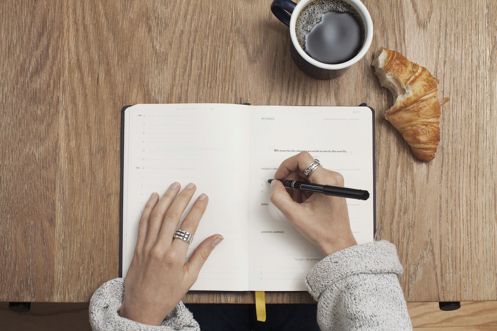 A writer working in a journal beside a cup of coffee